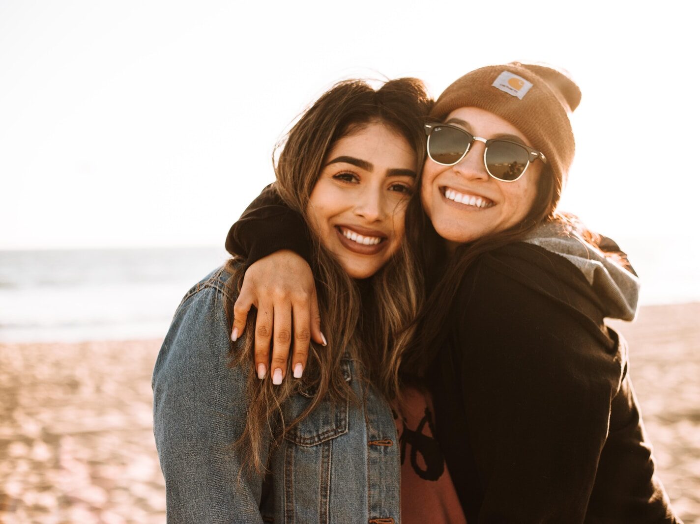 woman hugging other woman while smiling at beach